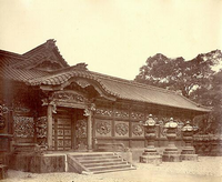 瓦屋根で豪華な装飾が施されている門の右側手前に、3つの大きな灯篭が並んでいる白黒写真