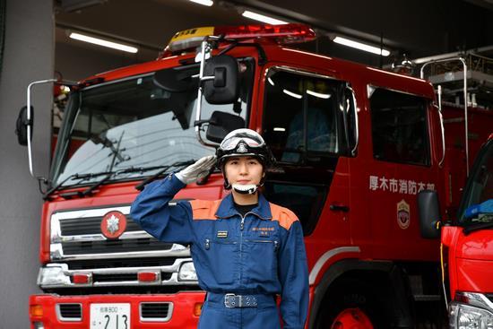 消防車の前で敬礼している消防署員の写真