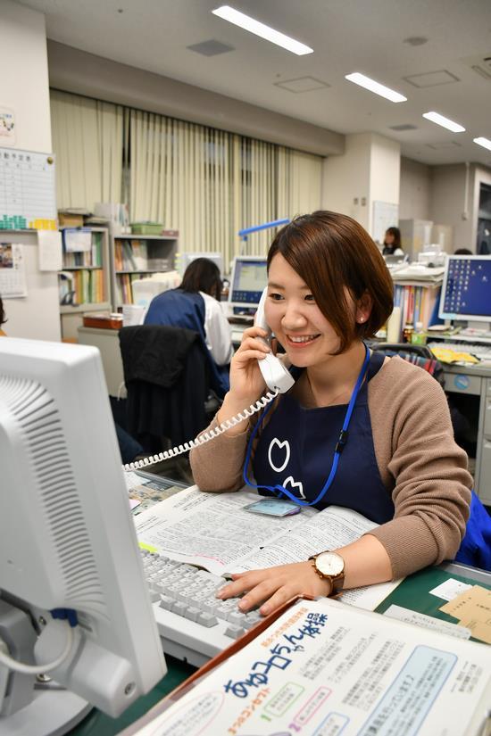デスクでパソコンを操作しながら電話応対をしている女性職員の写真