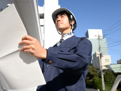 作業着を着てヘルメットを被った男性が図面の白い紙を広げている写真