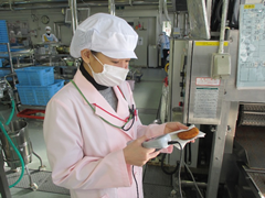 調理室にて白衣を着て白い帽子を被った女性が、食品の数値を機械を使って測っている写真