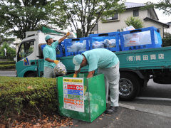 水色のポロシャツを着た男性2名がゴミ袋の回収をしており、トラックの荷台に積み込んでいる写真