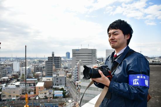 屋上から街を眺め、カメラを構えている男性職員の写真