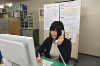 デスクに座り電話をかけている教育総務課女性事務職員の写真