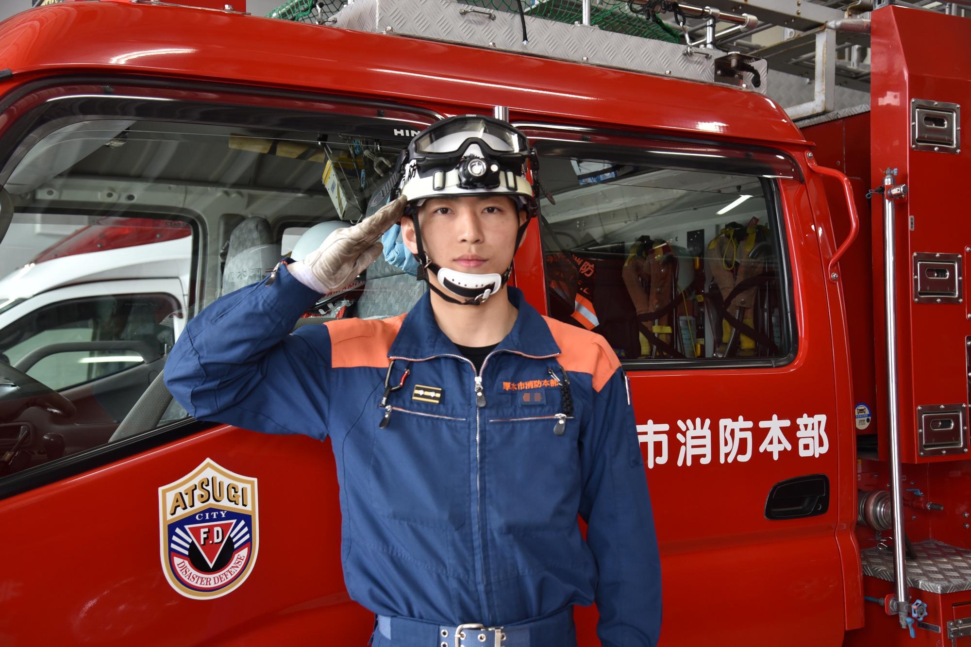 消防車の前で敬礼している男性消防署員の写真