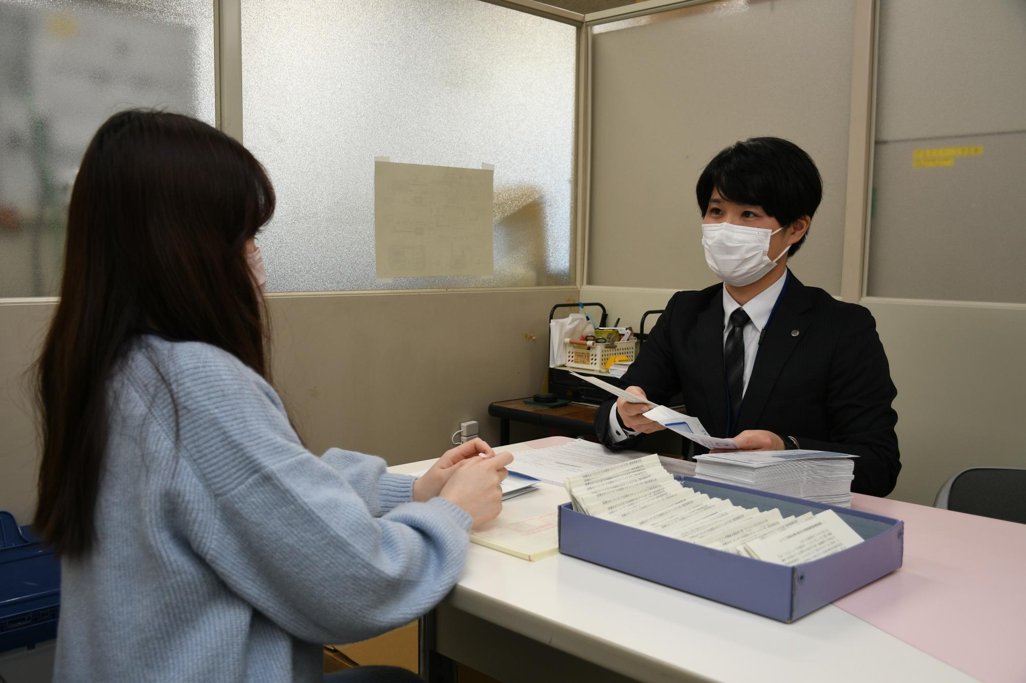 作業スペースで女性職員と一緒に通知の封入作業をしている男性職員の写真