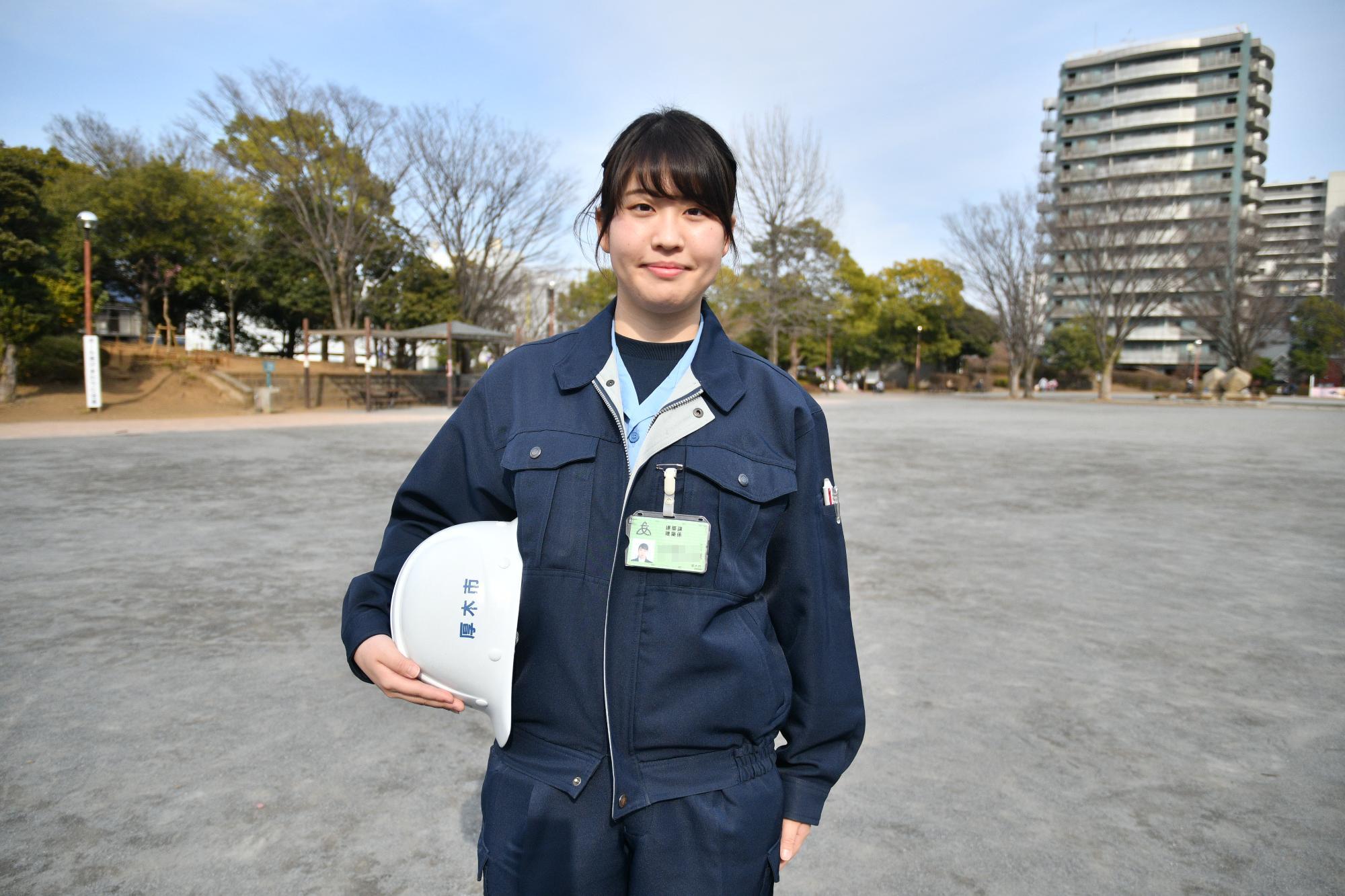 公園で作業着を着て笑顔で立っている建築職の女性職員の写真