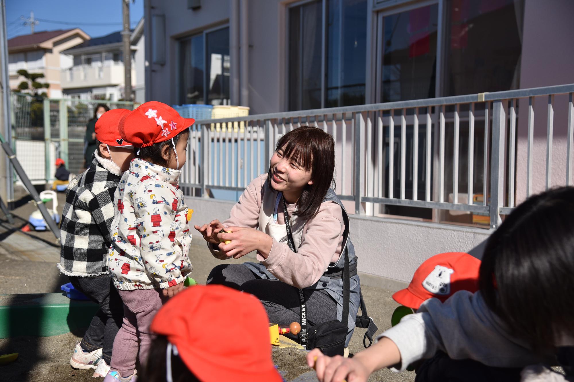 園庭で子どもたちと一緒に遊んでいる女性保育士の写真